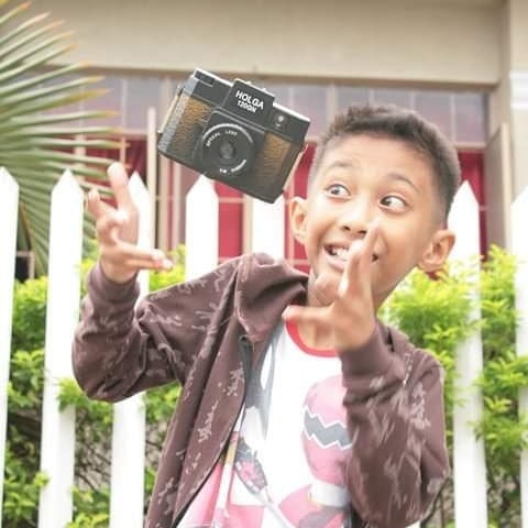 Emman Nimedez in a white t-shirt and brown jacket playing with a camera.